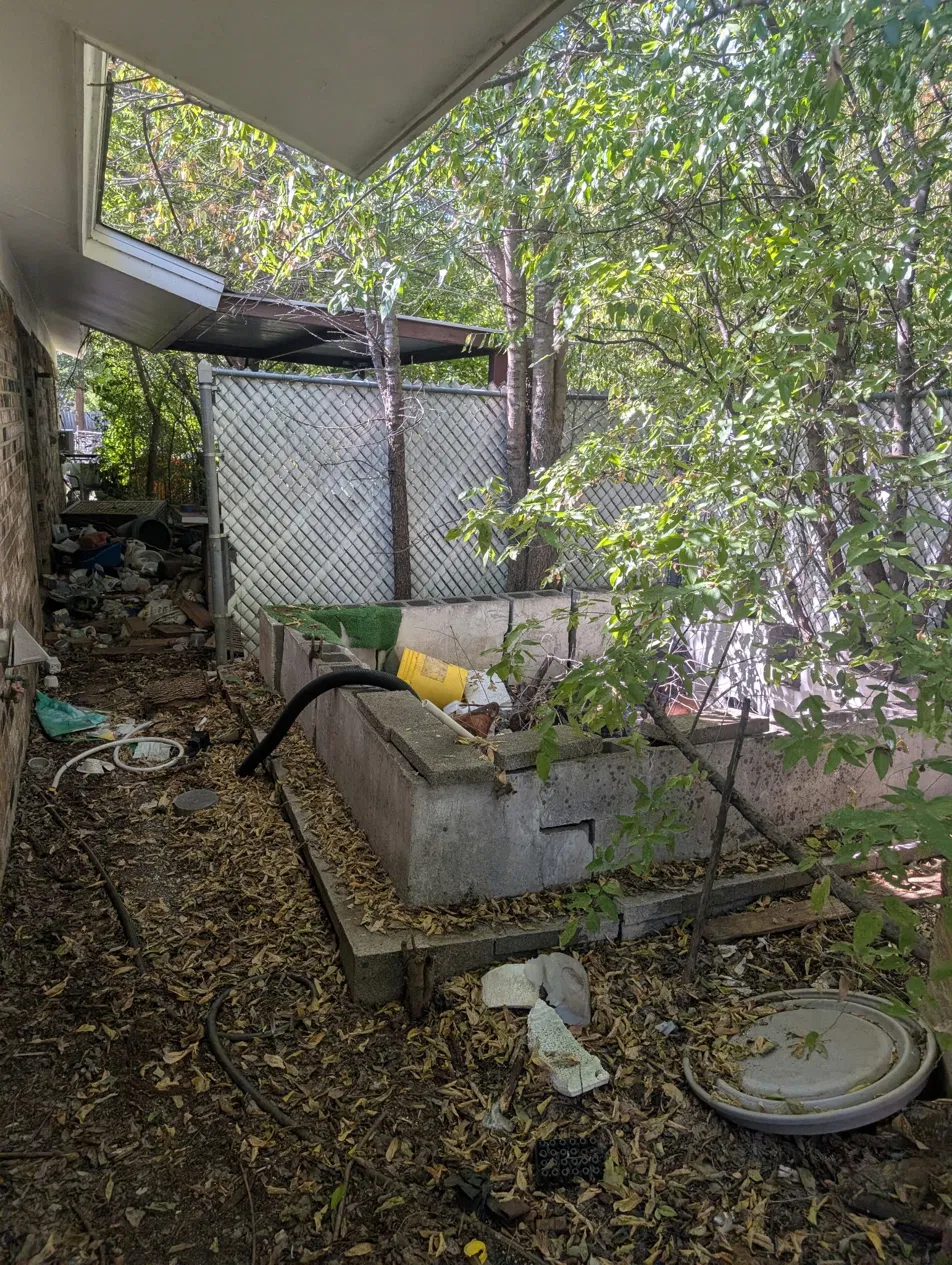 Distressed DFW rental property backyard before rehab, overgrown landscaping and debris
